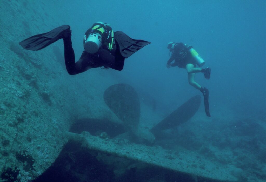 Scuba divers approaching propeller of ship wreck